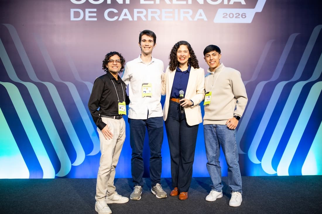 Três homens e uma mulher posam para foto em cima de um palco e com roupas sociais.