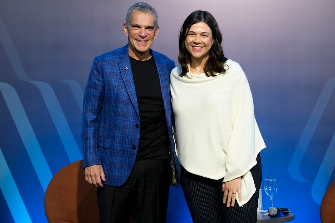 Um homem de blazer azul e cabelo grisalho e de uma mulher de roupa branca em cima de um palco.
